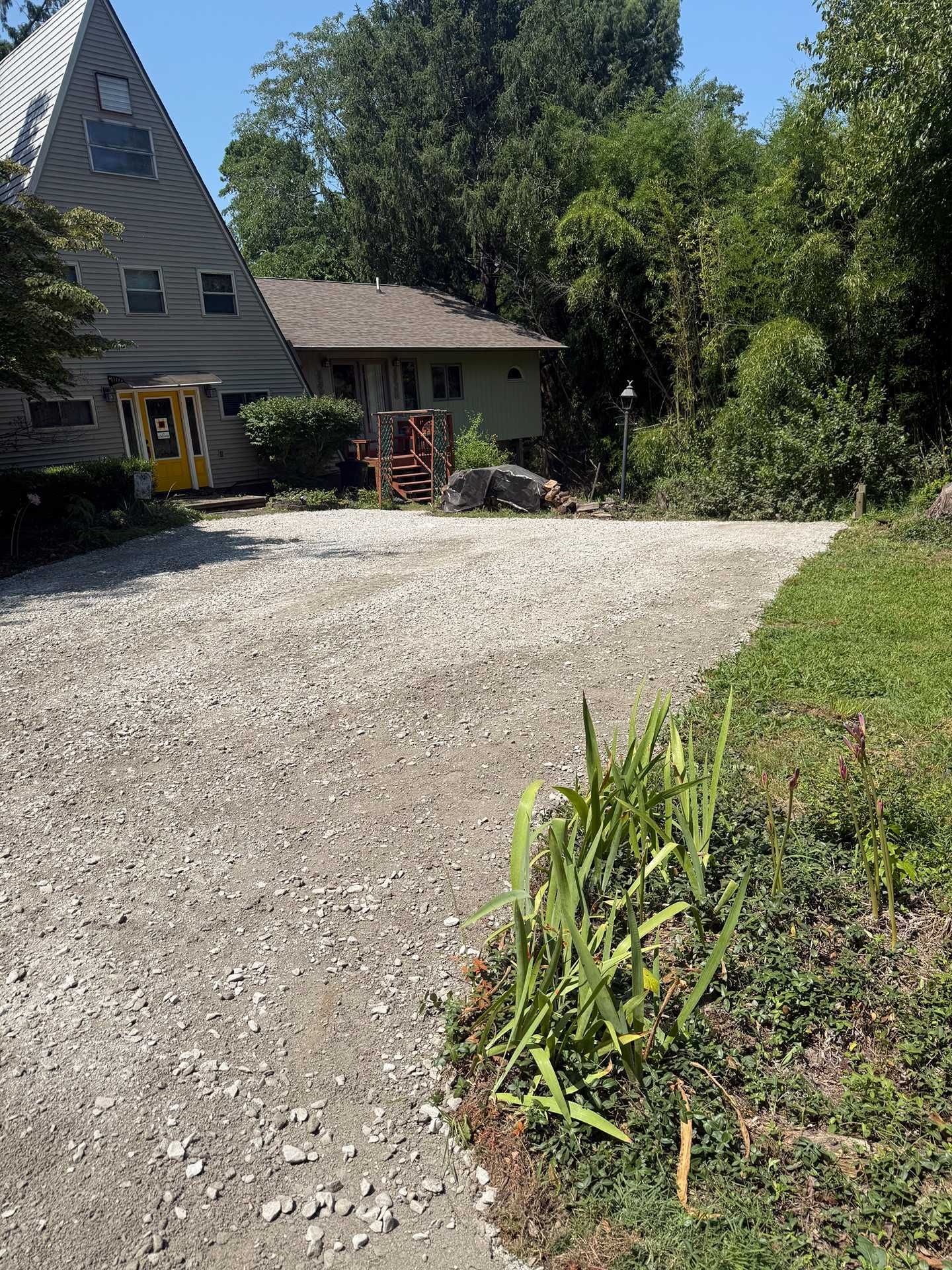Gravel driveway beside a house and lush green trees under a bright blue sky