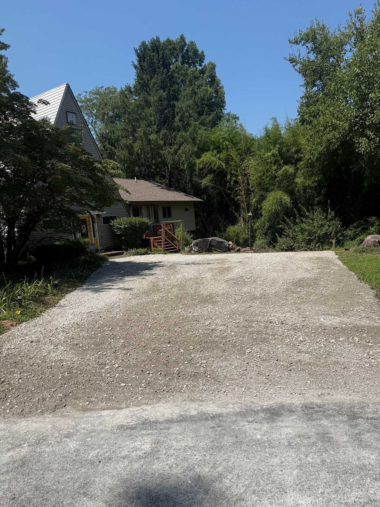 Gravel driveway leading to a small house with trees and a clear blue sky