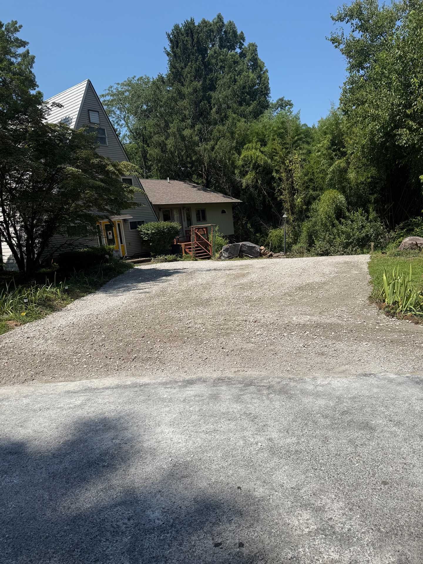 Gravel driveway leading to a house and trees on a sunny day