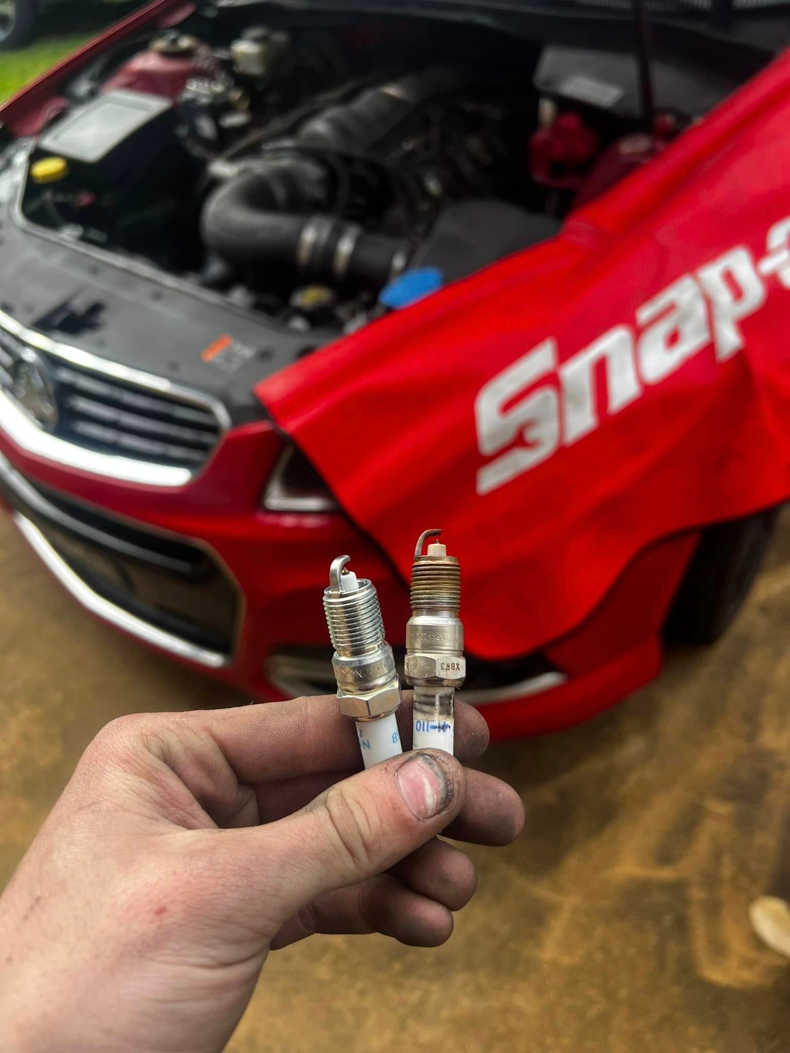 A Person Is Holding Two Spark Plugs In Front Of A Snap-on Car — MJ's Mobile Car Mechanic In Wollongong, NSW