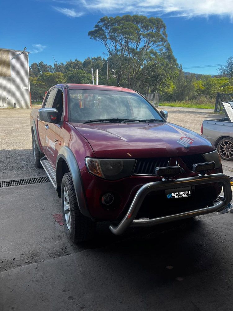 A Red Truck Is Parked In A Parking Lot Next To A Building — MJ's Mobile Car Mechanic In Wollongong, NSW