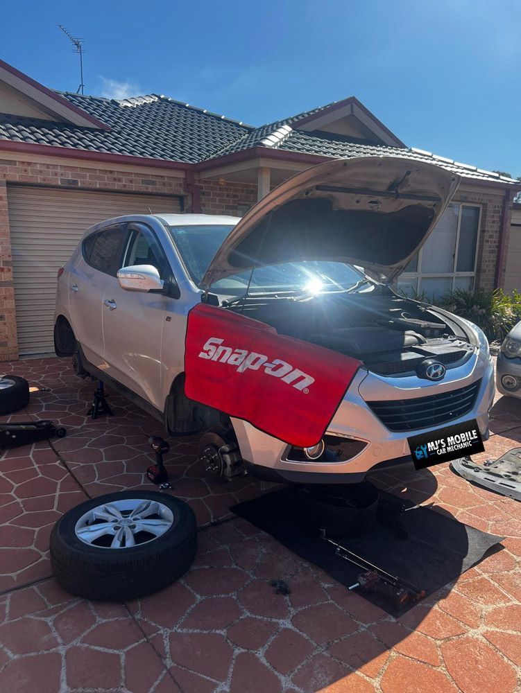 A Car With The Hood Up Is Sitting On A Lift In Front Of A House — MJ's Mobile Car Mechanic In Wollongong, NSW