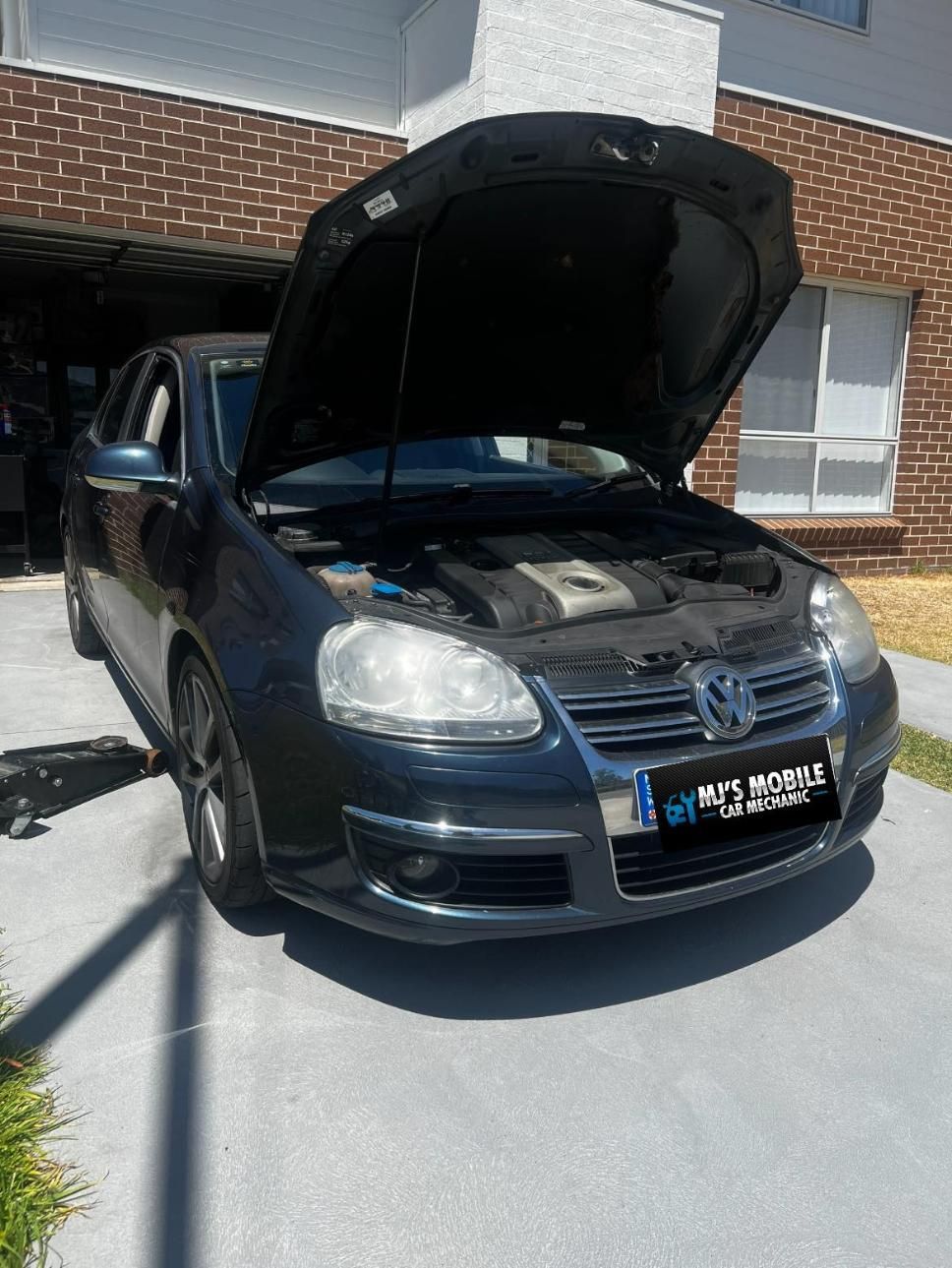 A Black Car With The Hood Up Is Parked In Front Of A Brick Building — MJ's Mobile Car Mechanic In Mount Annan, NSW