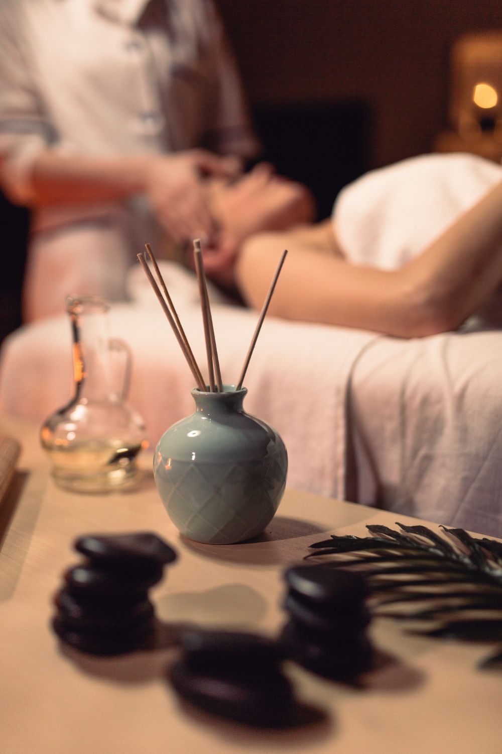 Una mujer recibe un masaje en un spa mientras un jarrón con palos dentro reposa sobre una mesa.