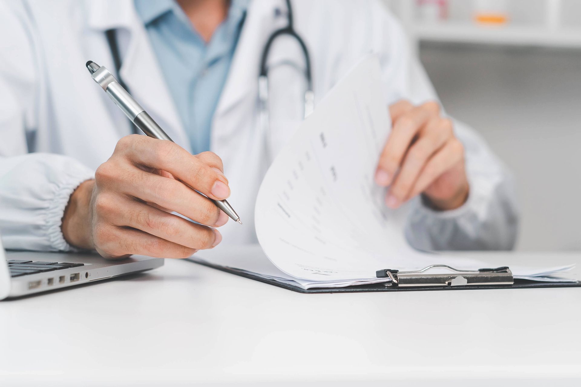 Male doctor in white coat signing papers at a desk.