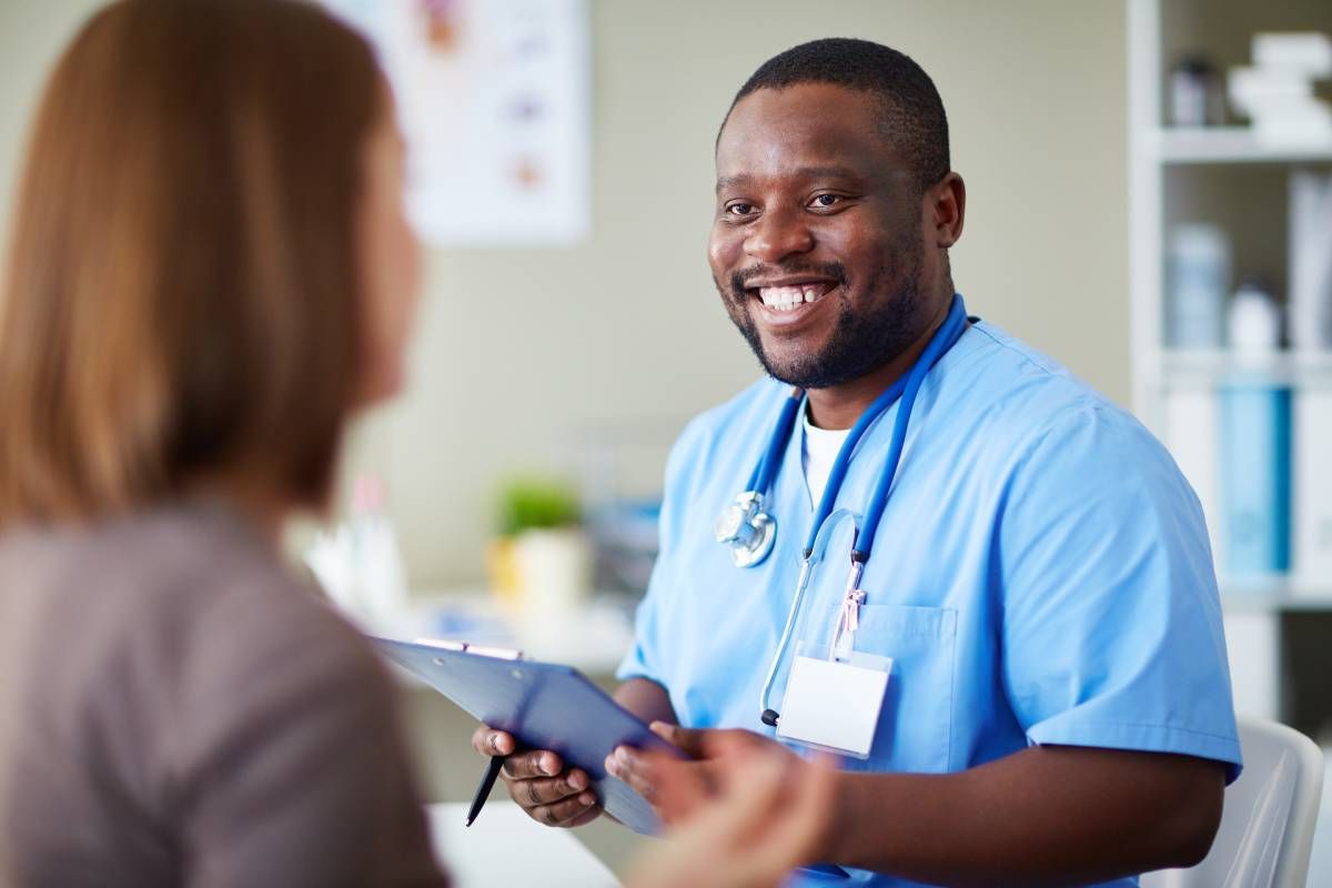 Smiling nurse practitioner holding a clipboard and talking to a patient.