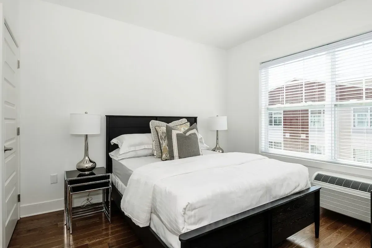 A bedroom with a bed , two lamps , and a window.