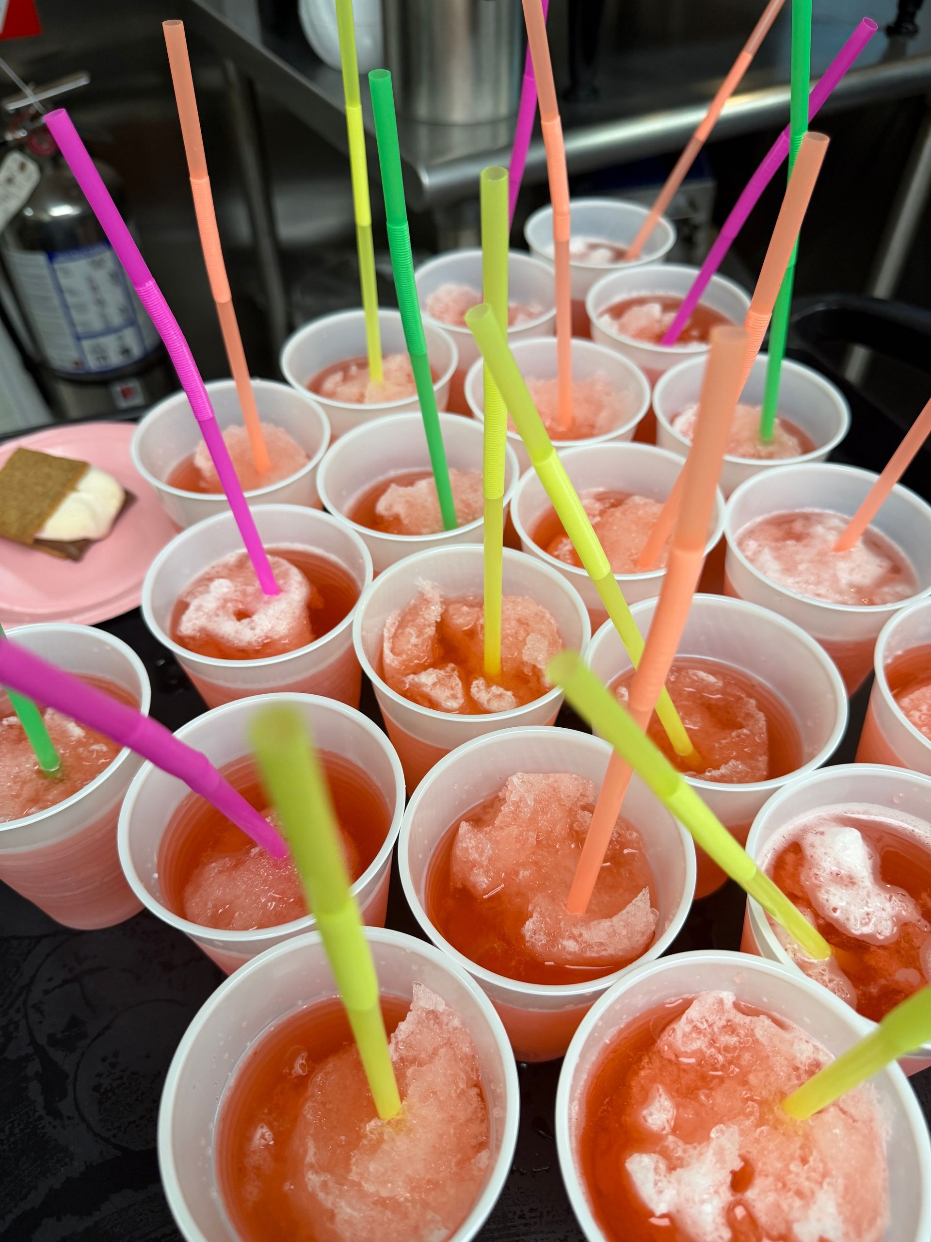 Many plastic cups of orange and pink shaved ice with colorful straws on a tray