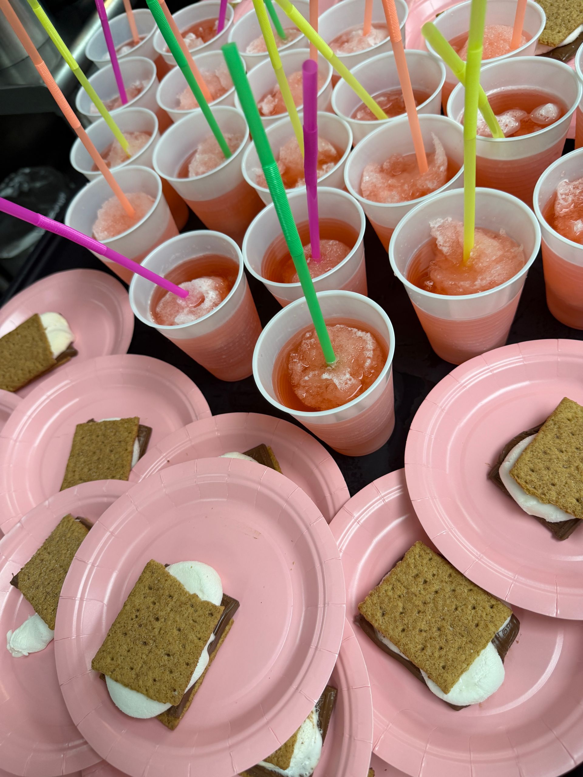 Pink trays with ice cream sandwiches and cups of orange dessert topped with colorful straws