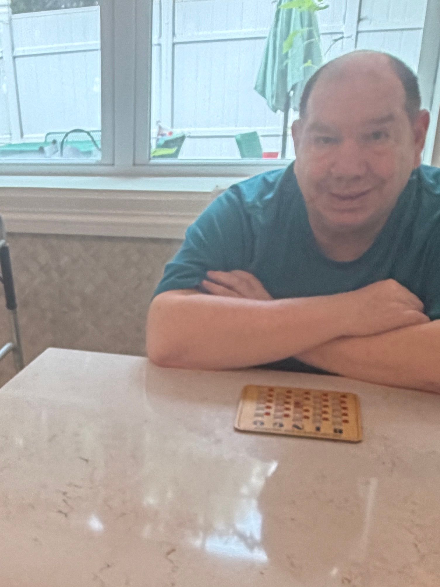 Man seated at a table in a bright room, resting his arms and looking toward the camera.