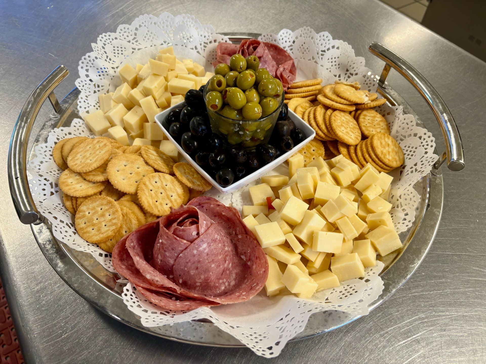Charcuterie platter with crackers, cubed cheese, salami, olives, grapes, and cucumber slices on a lace doily