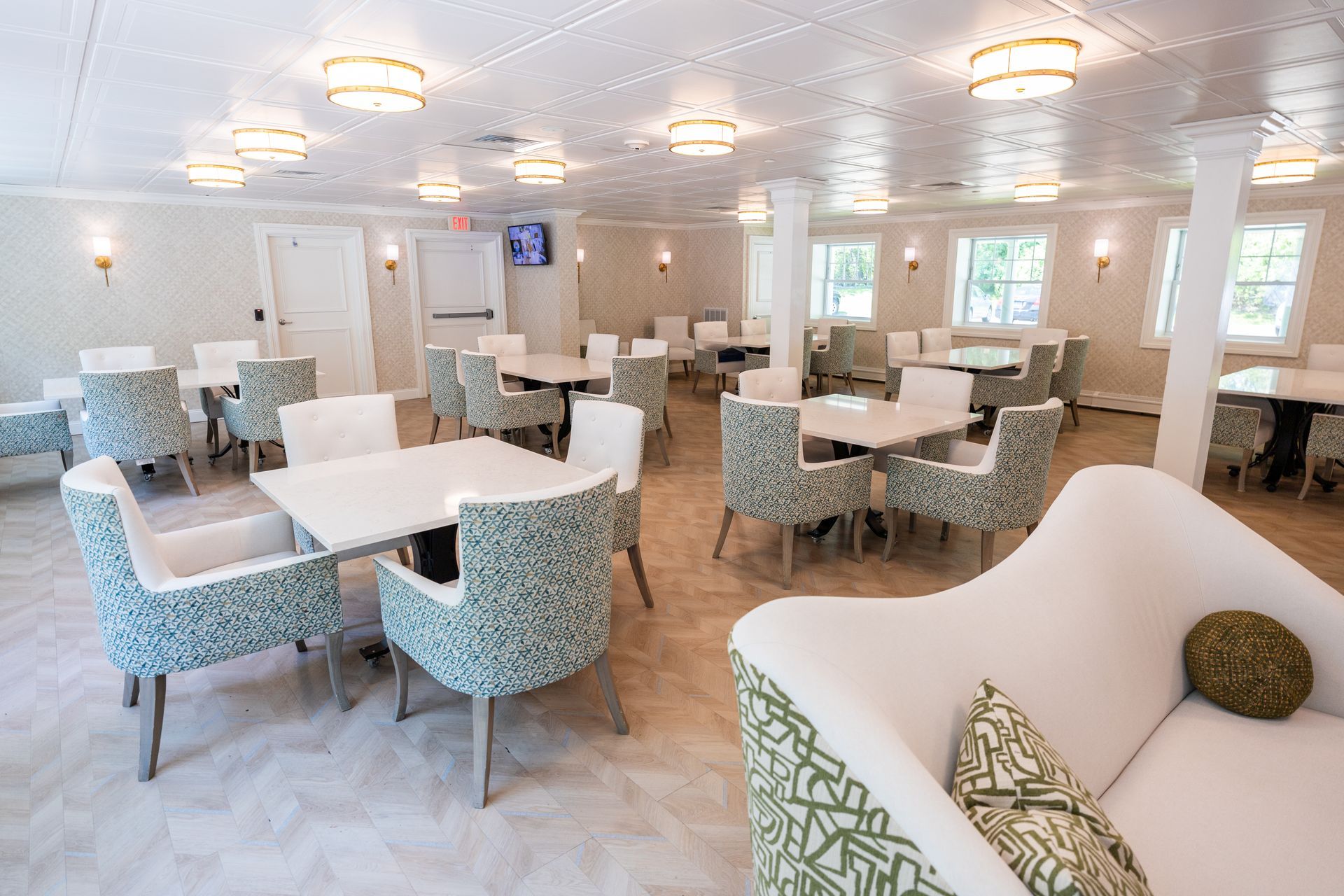Bright dining room with white tables, patterned chairs, and large windows in a modern indoor setting