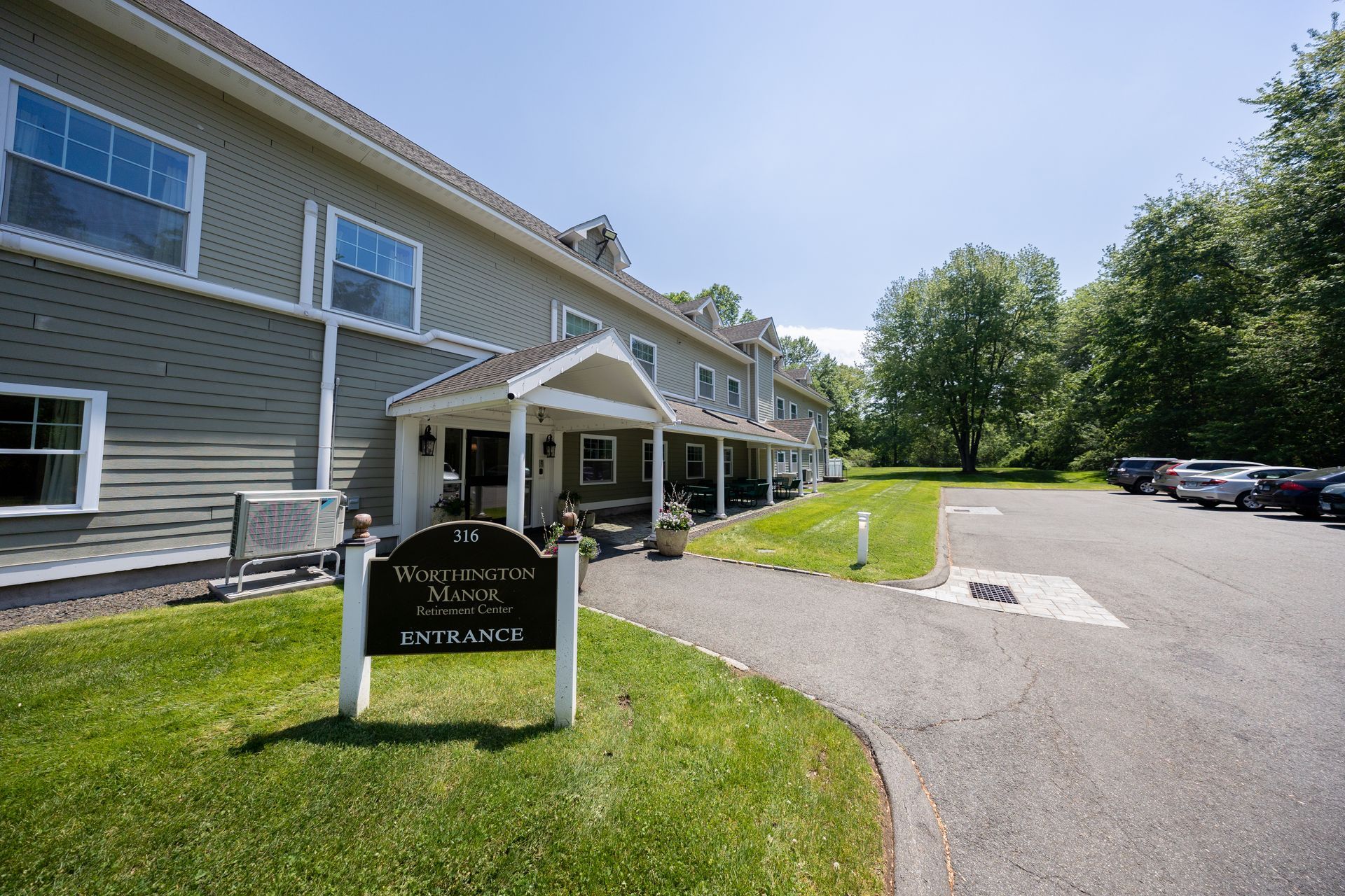 Building entrance with covered walkway, sign, lawn, and parking lot on a sunny day