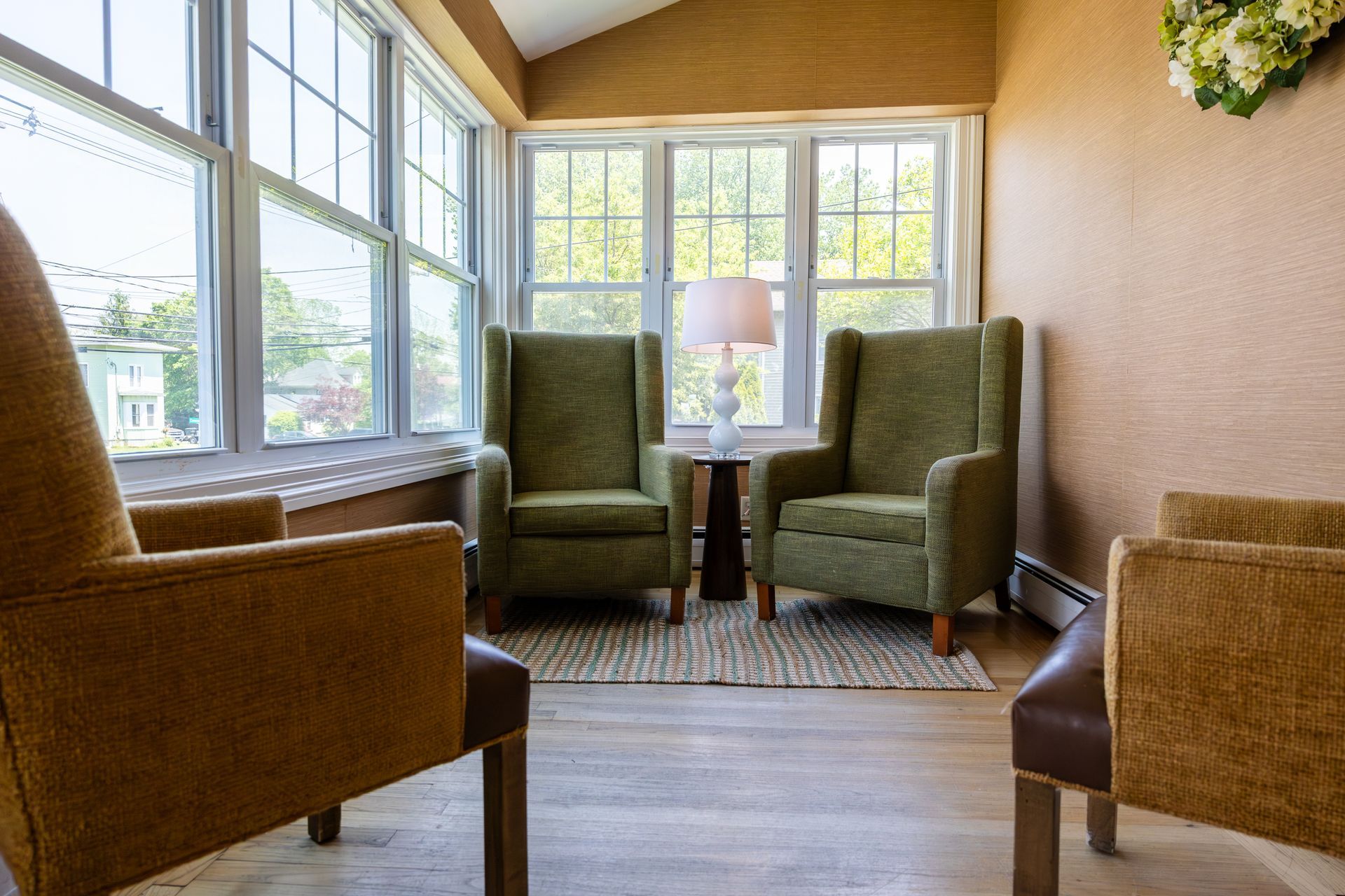 Cozy sunroom with wicker chairs, a lamp, and large windows overlooking greenery.