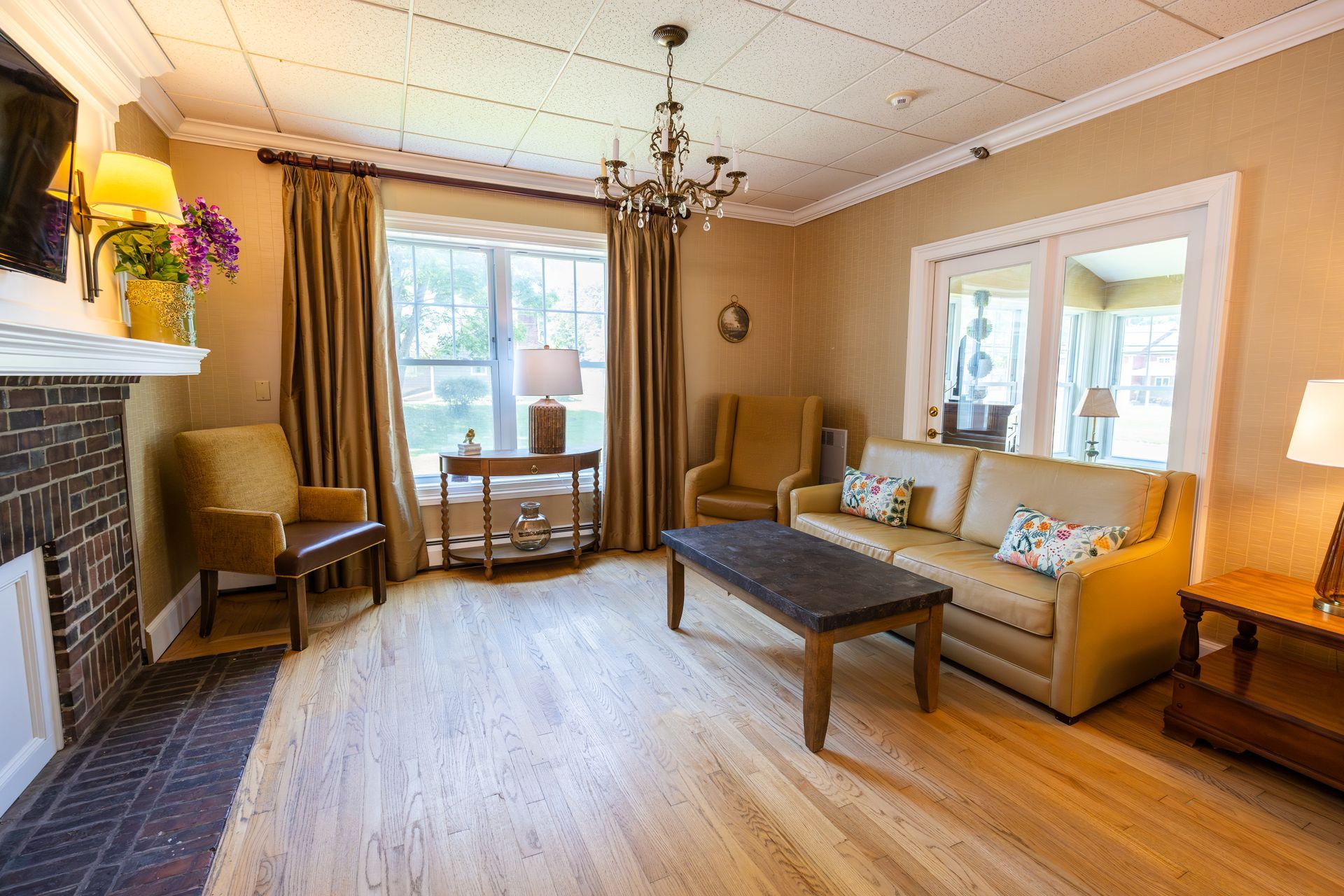 Cozy living room with beige sofa, coffee table, fireplace, chandelier, and large window.