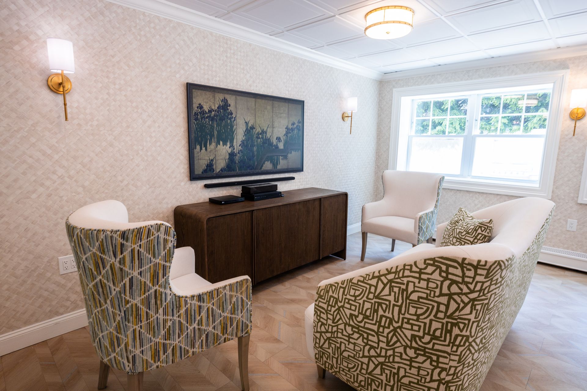 Bright living room with patterned chairs, sofa, TV, and large window