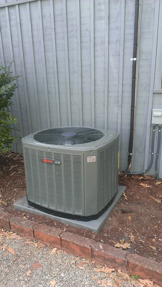 Outdoor HVAC condenser unit beside a wooden fence and brick edging