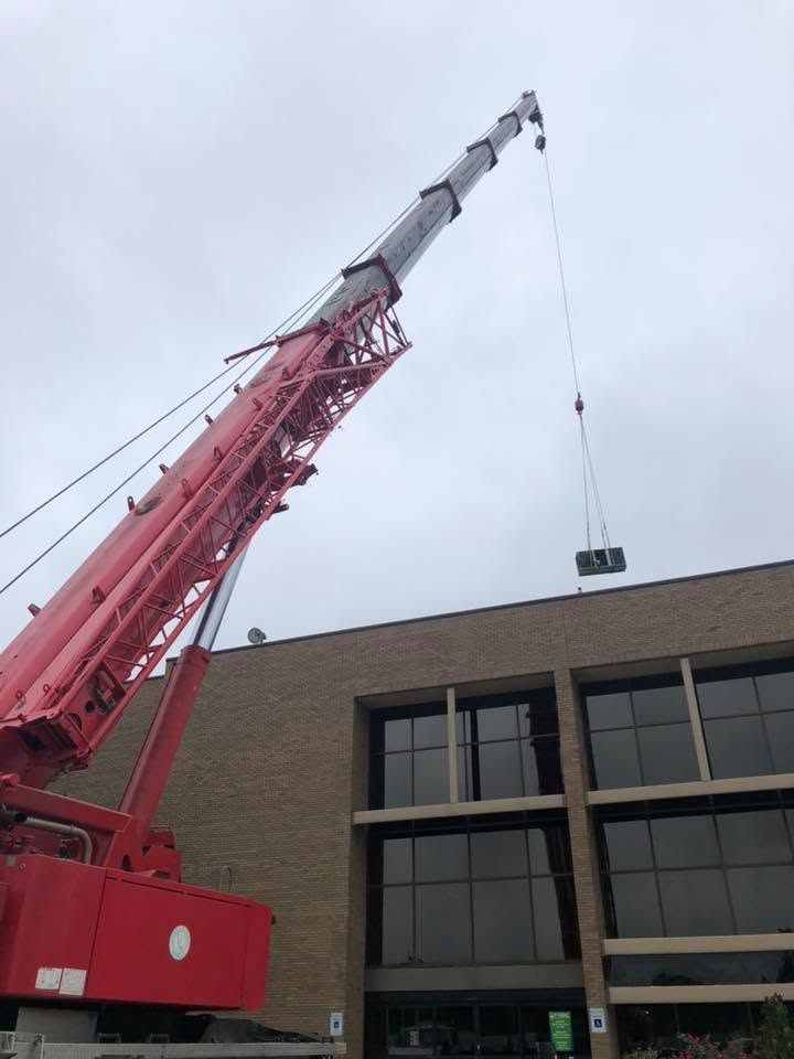 Red crane hoisting a load beside a brick building under a cloudy sky.