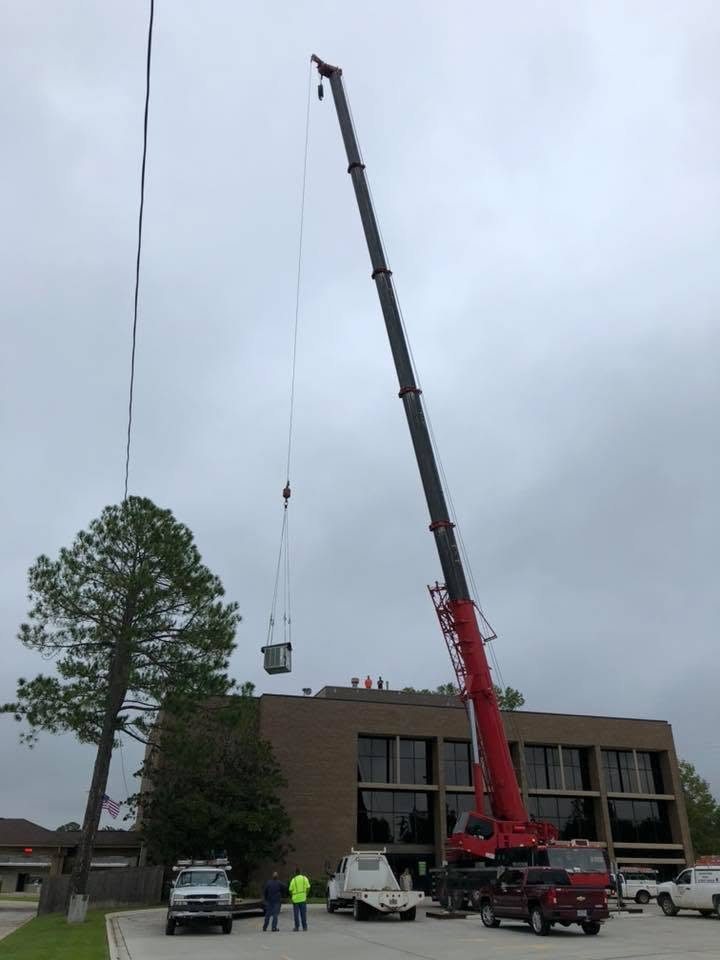 Crane lifting a bucket beside a building, with workers and parked vehicles below.