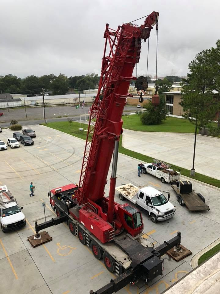 Red crane truck with extended boom parked beside white trucks in a paved lot