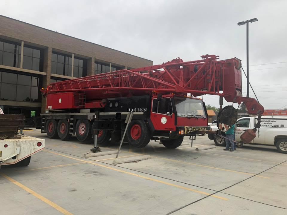 Red crane truck parked in a lot beside a building, with a few people standing nearby.