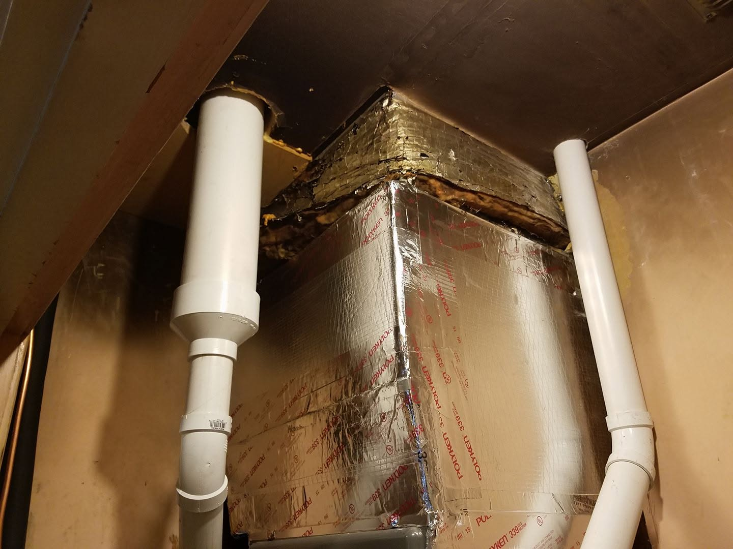 Rusty metal duct corner with two white PVC pipes inside a cabinet or ceiling space