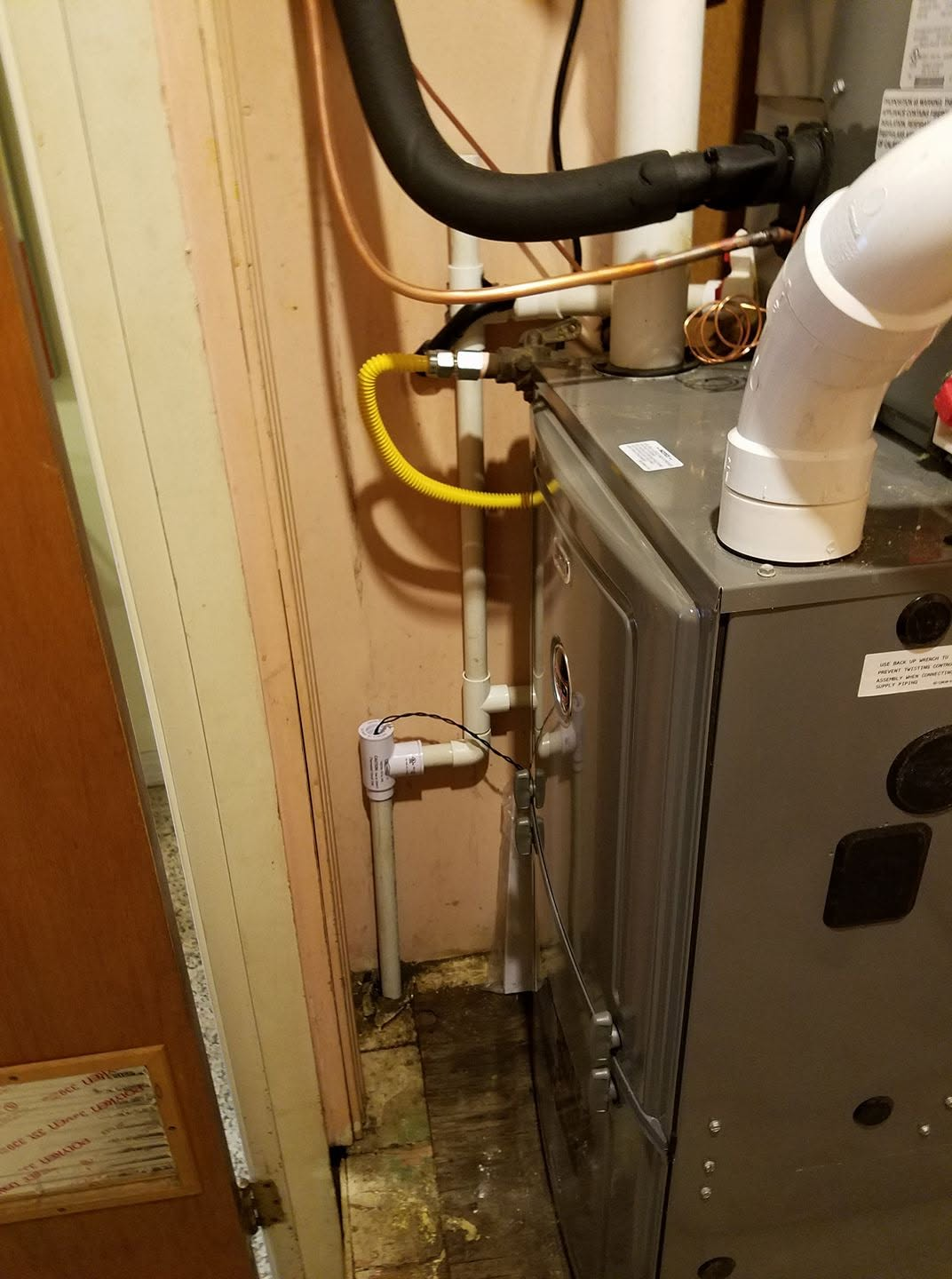 Gas furnace beside a wall, with yellow and black pipes in a tight utility closet.