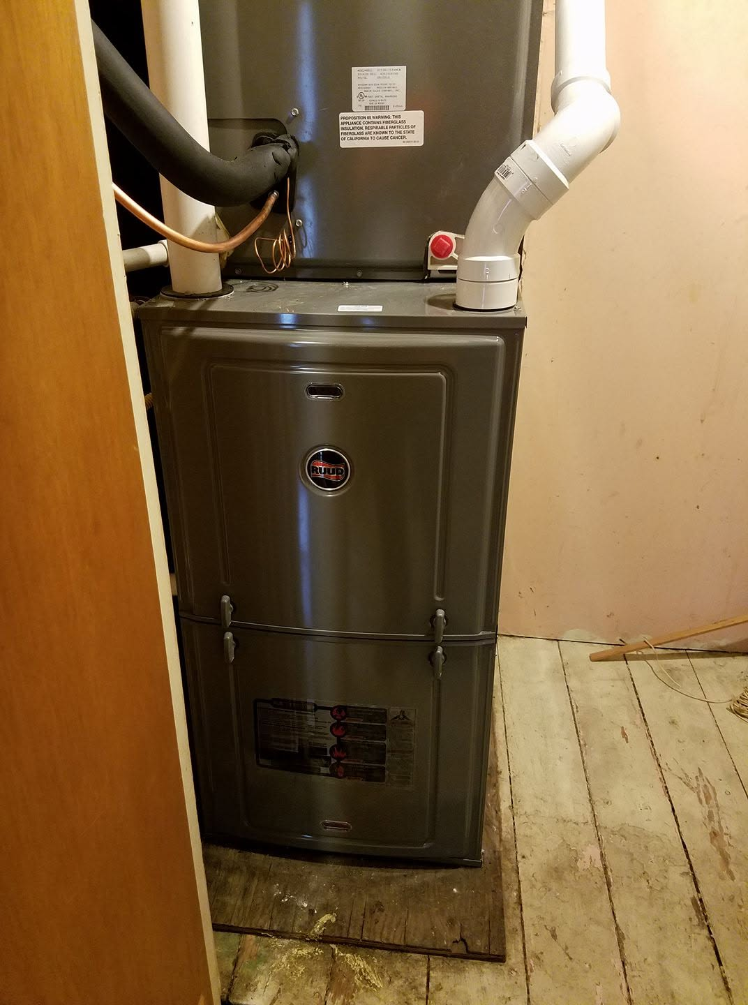 Gray furnace with white vent pipes installed in a narrow utility closet.