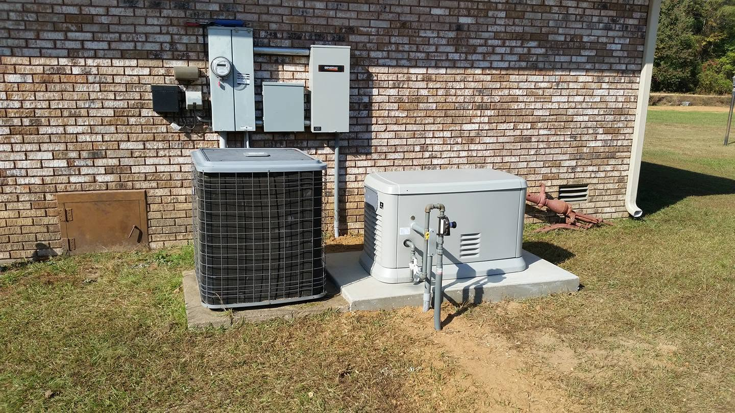Outdoor HVAC unit and electrical boxes beside a brick building on a grassy lawn.