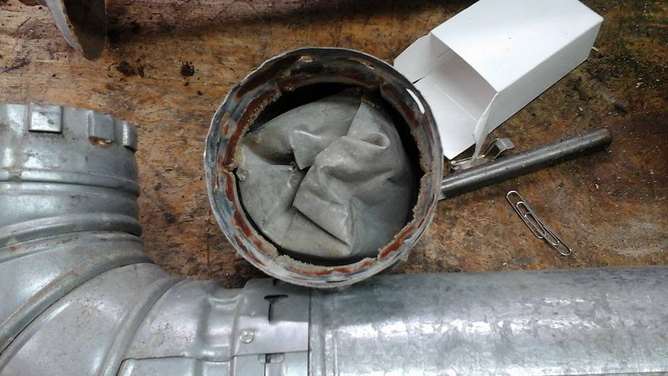 Metal ductwork with a circular opening stuffed with gray cloth beside a white box on a work surface