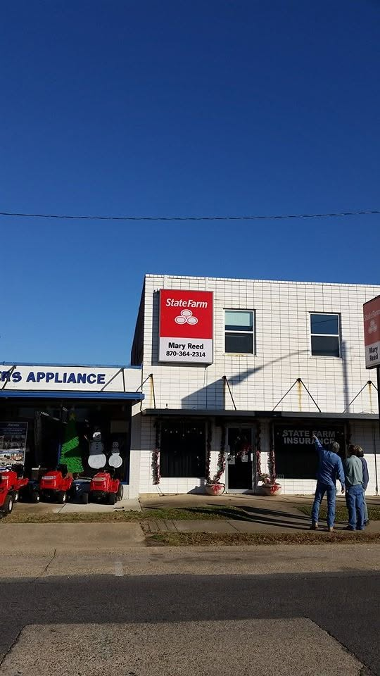 Storefronts along a street, including an appliance shop and a red sign building, with two people standing outside.