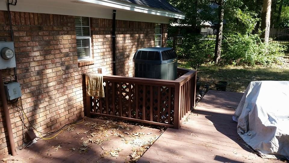 Brick house patio with wooden railing, grill, and covered furniture in a shaded yard