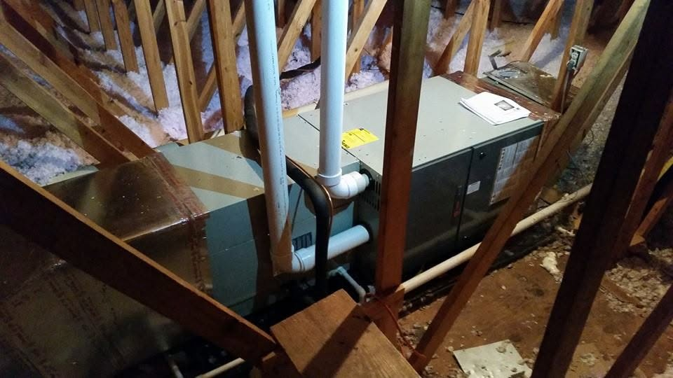 Furnace and pipes in an unfinished attic, framed by exposed wooden beams.