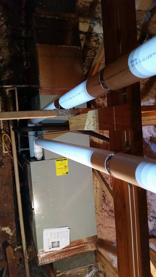 Attic crawlspace with two white pipes and a gray HVAC unit under exposed wooden beams.