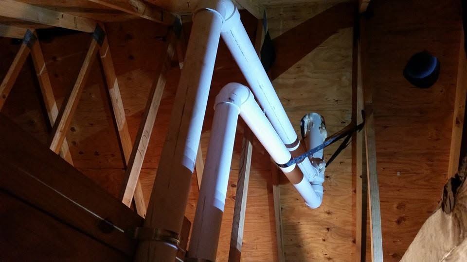 White PVC pipes and ducts run through a wooden attic framing.