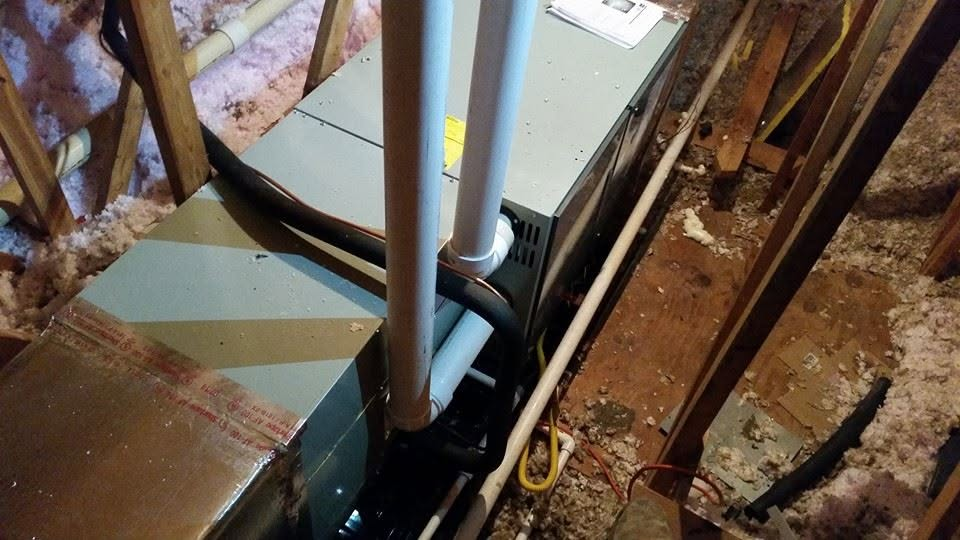Open HVAC unit with exposed pipes in a cluttered attic space