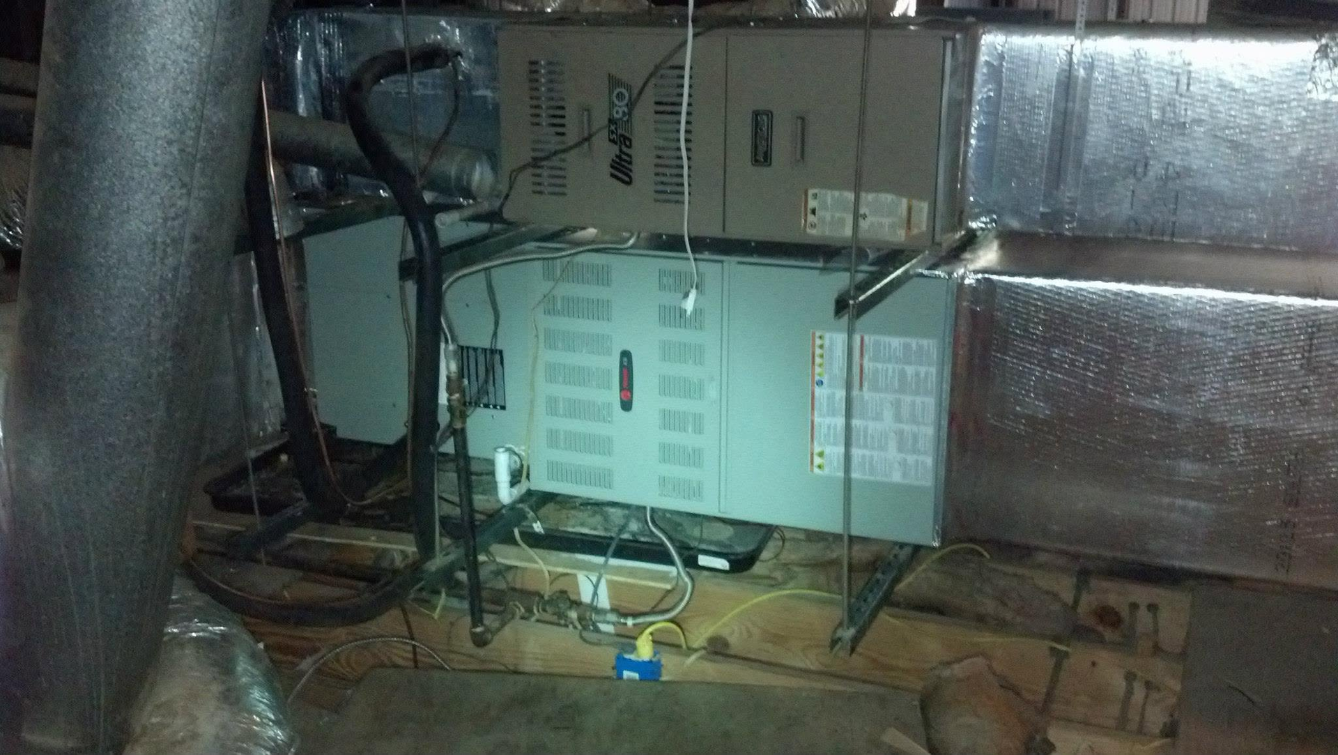 Utility equipment and wiring inside a metal-walled crawl space, with boxes and pipes on the floor.