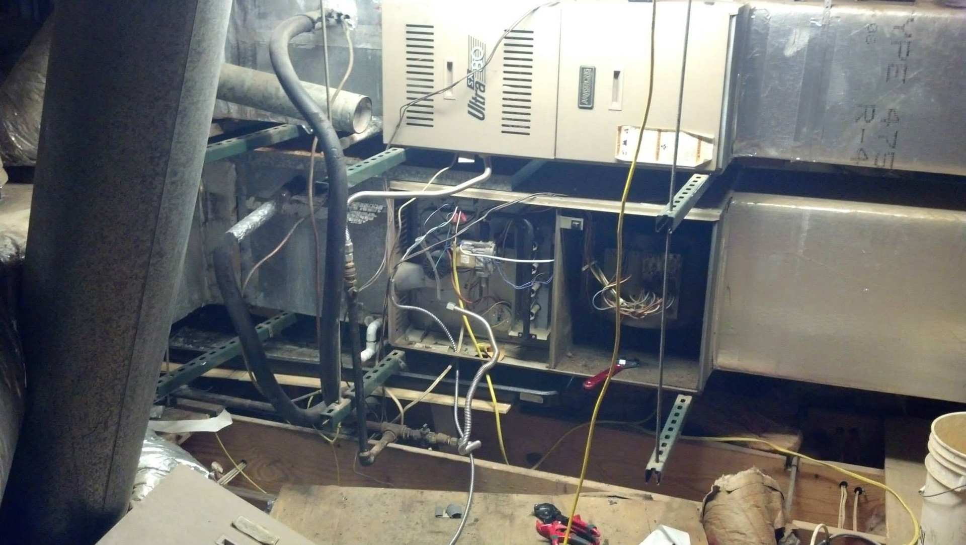 Exposed HVAC ductwork and wiring in a ceiling crawlspace, with tools and debris below.