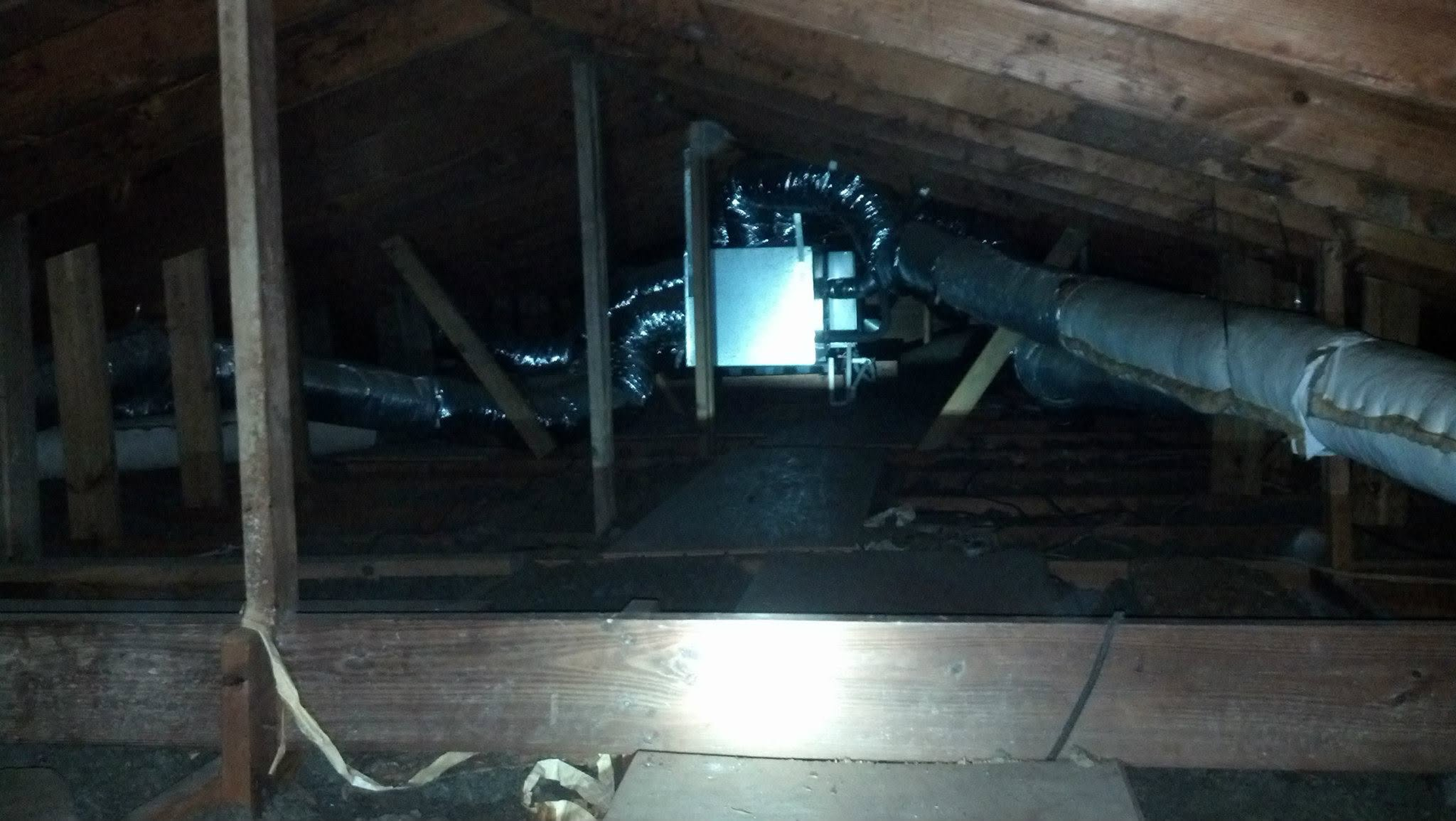 Attic crawlspace with exposed beams, ducts, and a bright light in the center