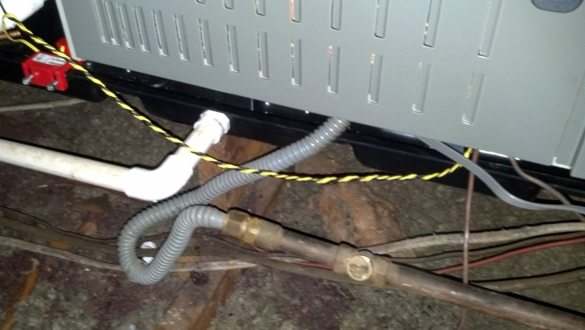 Tangled hoses and wires under an appliance on a dark floor