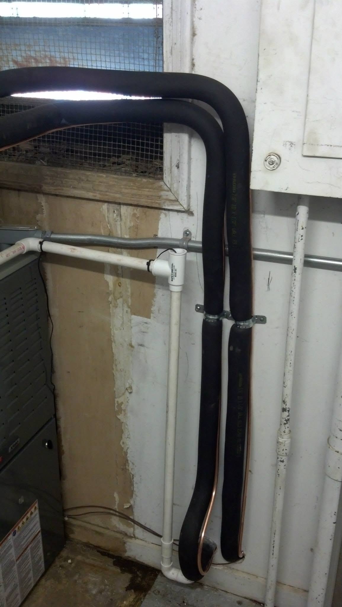Black bent pipes mounted on a white wall with an old window and exposed piping in a utility area