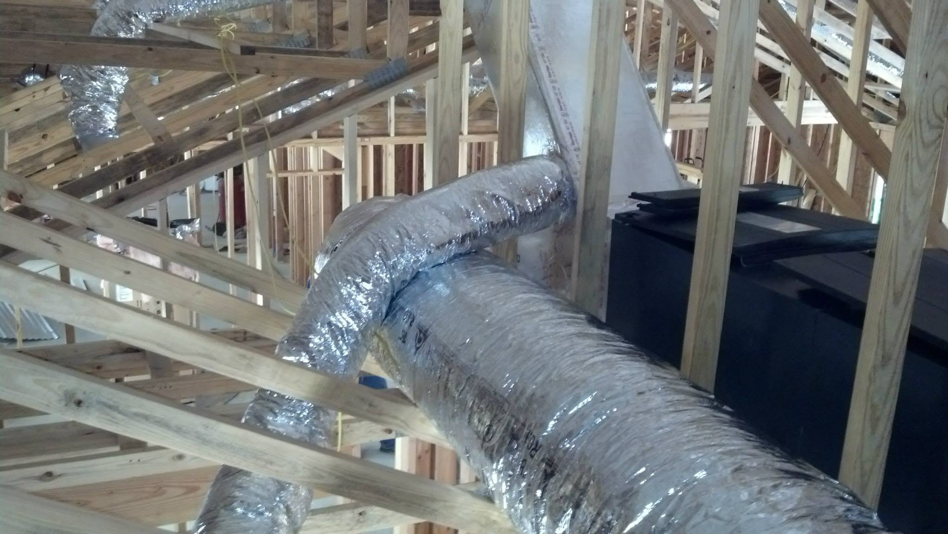 Foil-wrapped HVAC ductwork running through an unfinished wooden house framing under construction