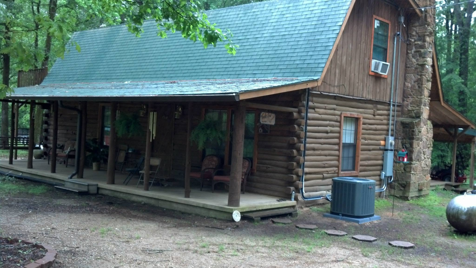 Rustic log cabin with a green roof and covered porch in a wooded yard