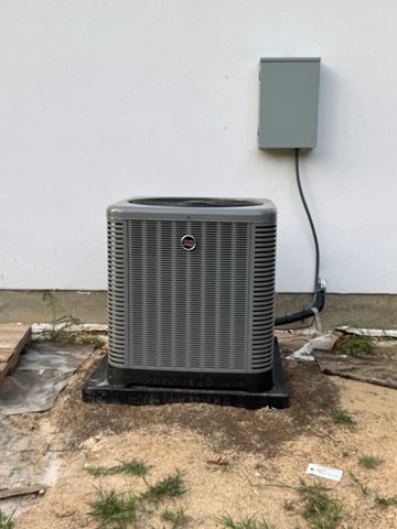 Outdoor HVAC condenser unit beside a wooden fence and brick edging