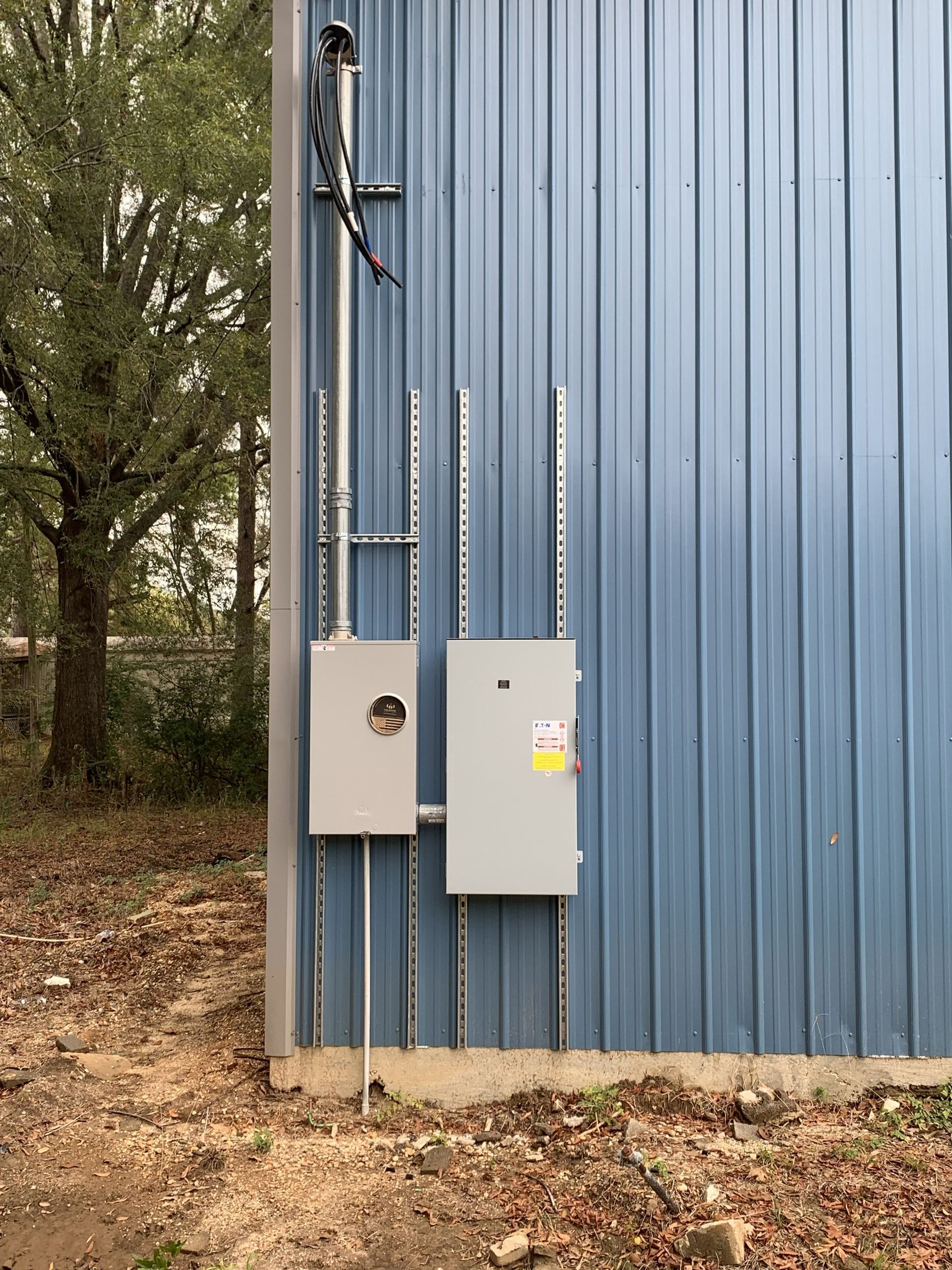 Open electrical panels and meter boxes mounted on a brick house exterior.