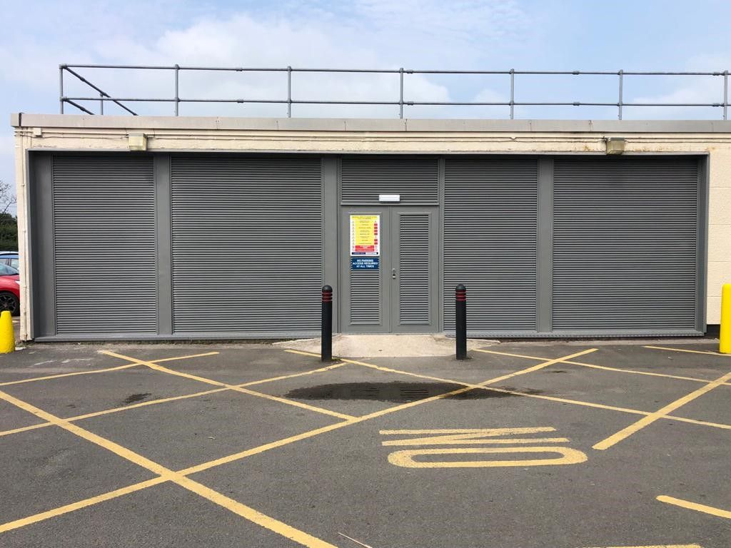 A building with a fence on top of it is in a parking lot.