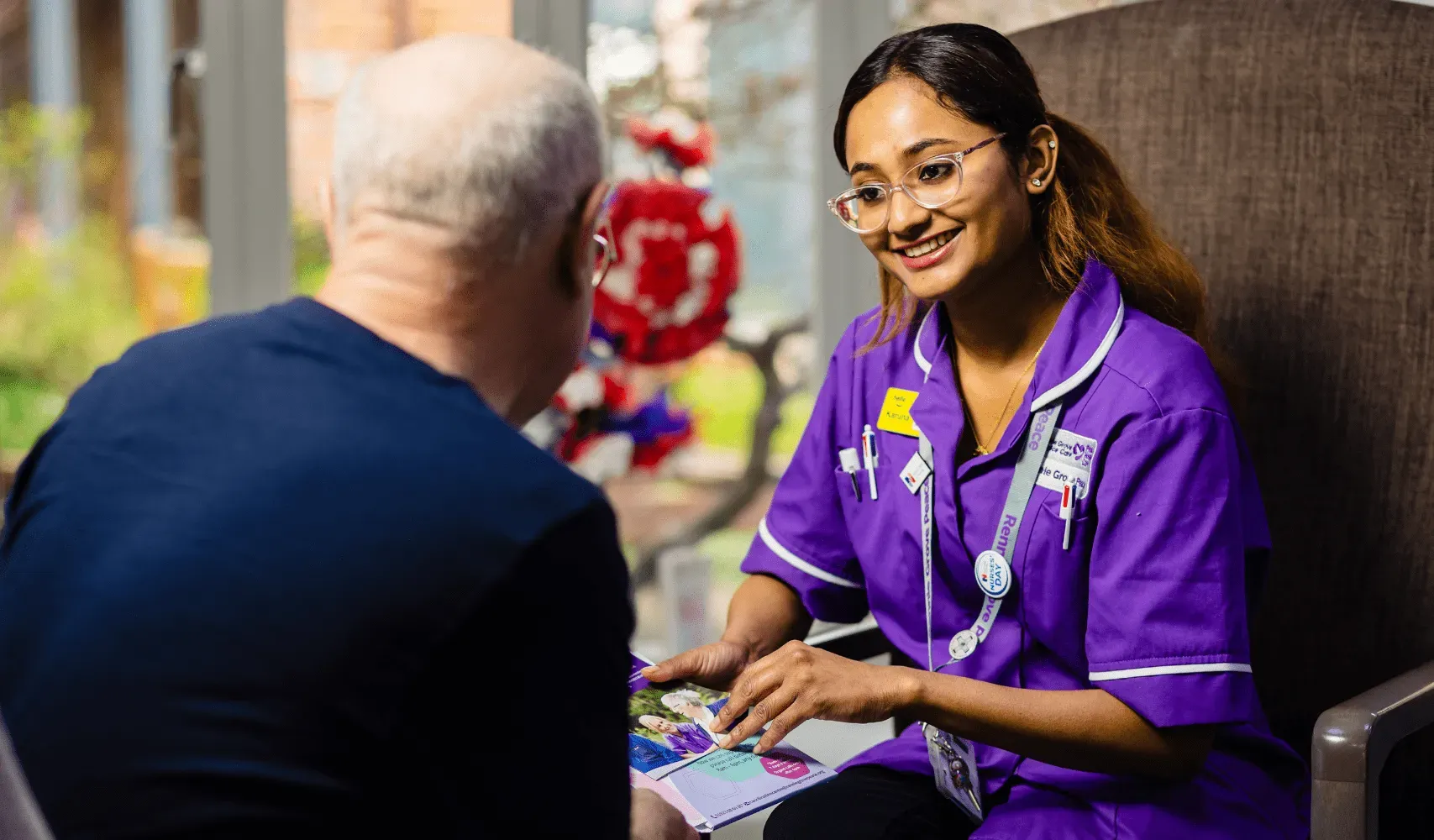 A nurse is talking to an elderly man in a chair.