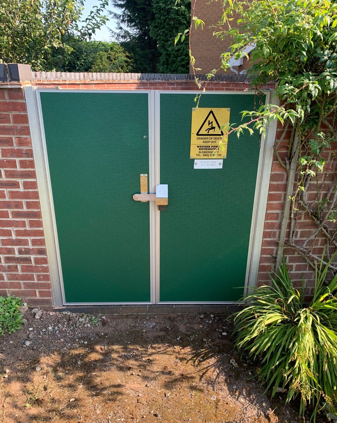 A green door with a yellow warning sign on it is next to a brick wall.