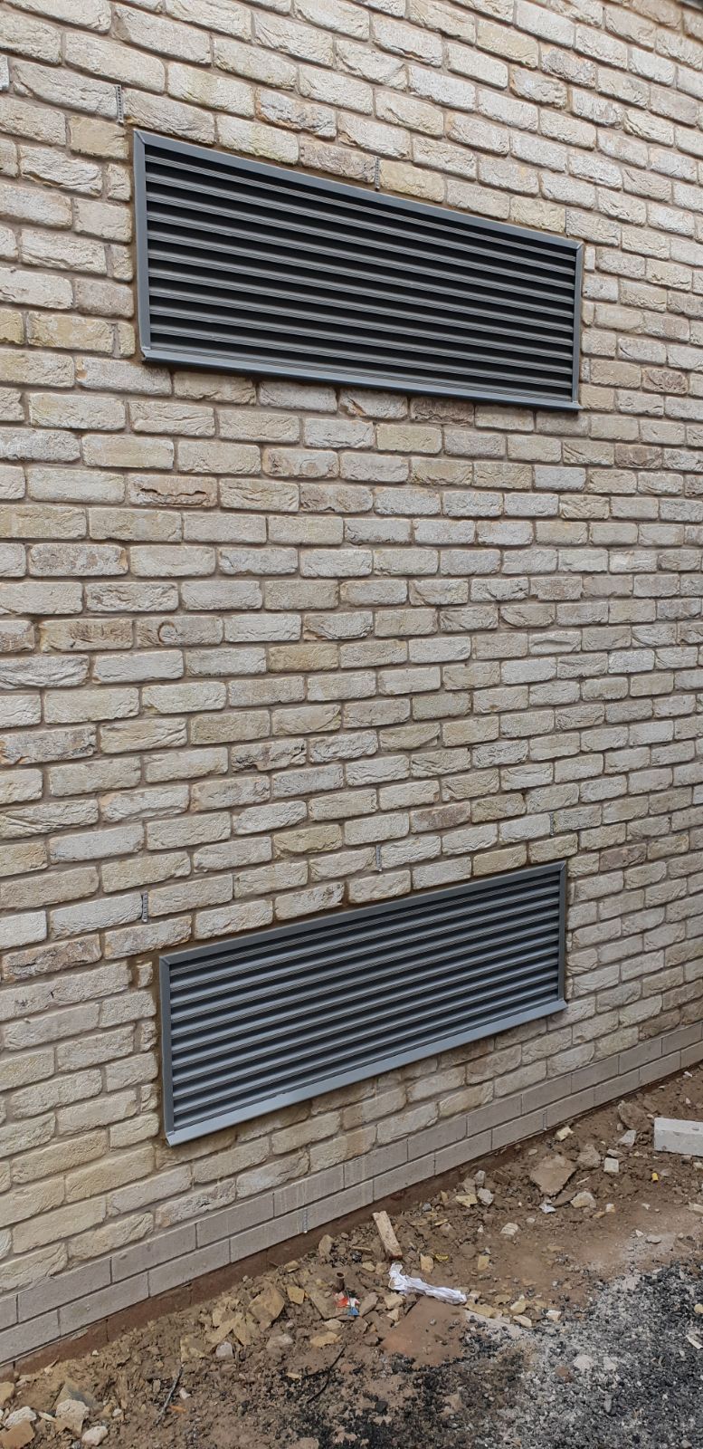 A brick wall with three metal vents on it.