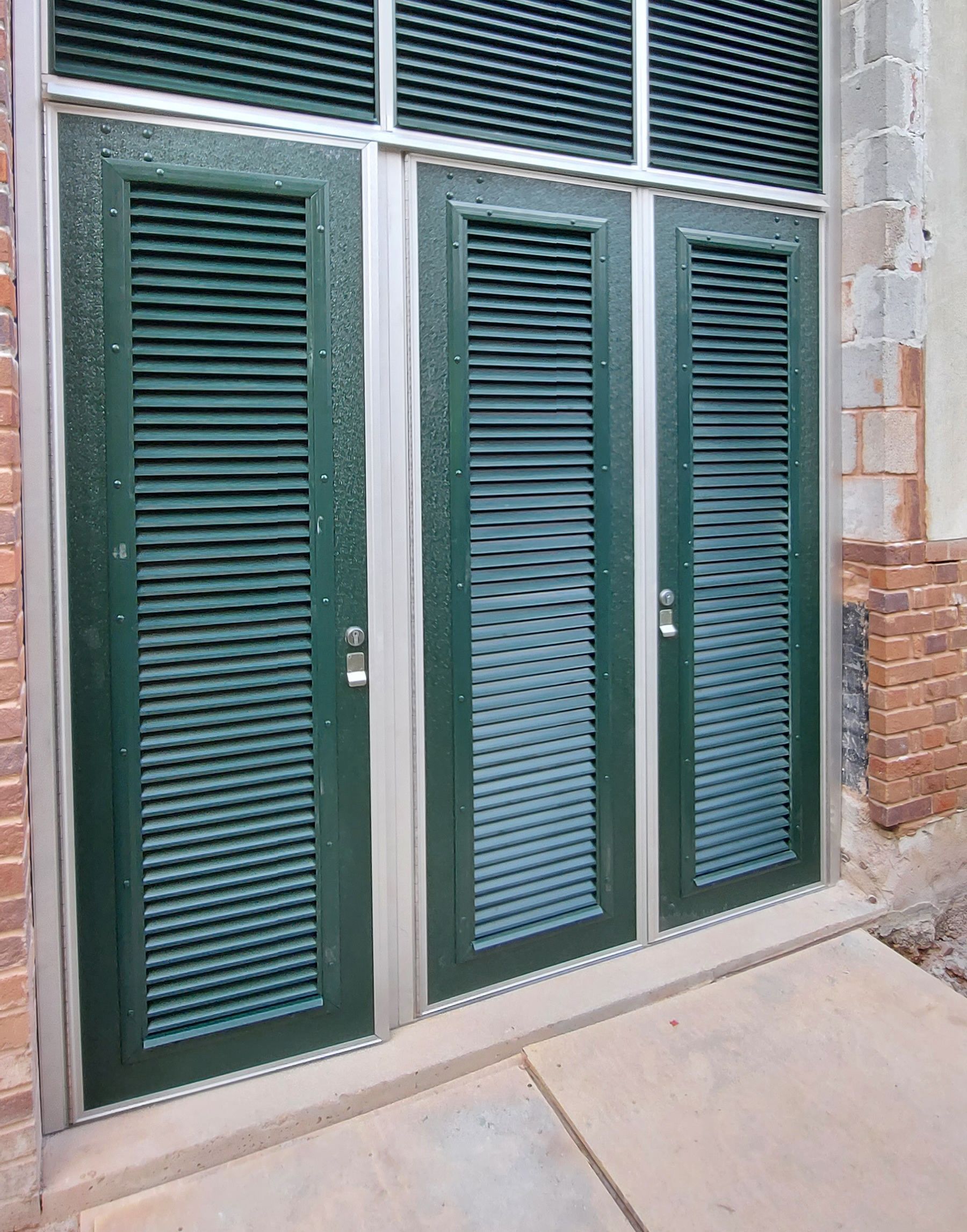 Three green doors with shutters on a brick building